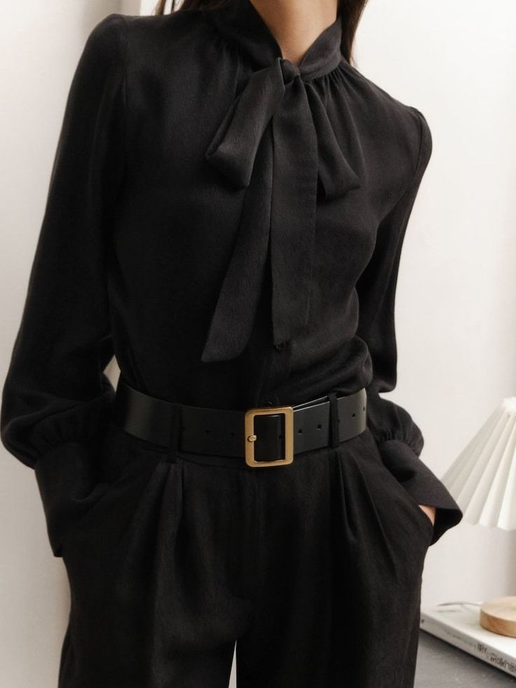 Person wearing a black pussy bow blouse and black pants with a wide belt