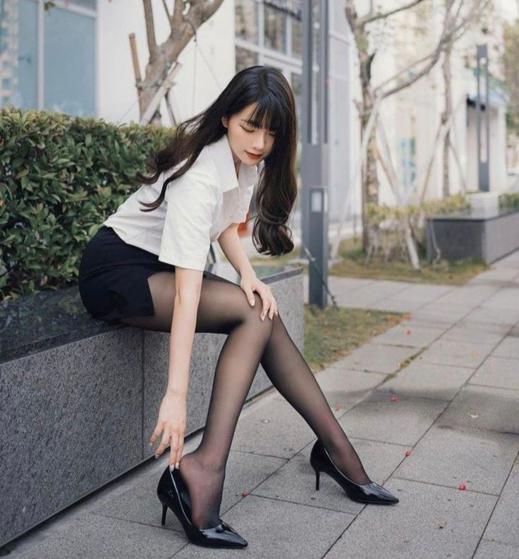 Woman in a white shirt and black skirt with tights and high heels outdoors
