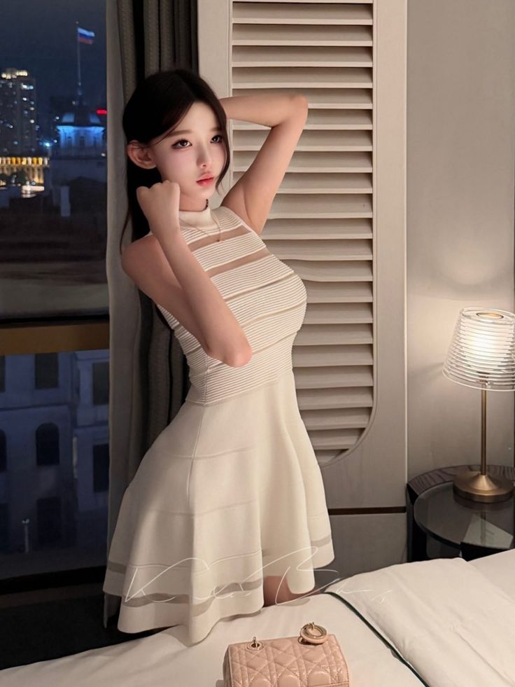 Woman in a white dress posing in a room with a city view at night
