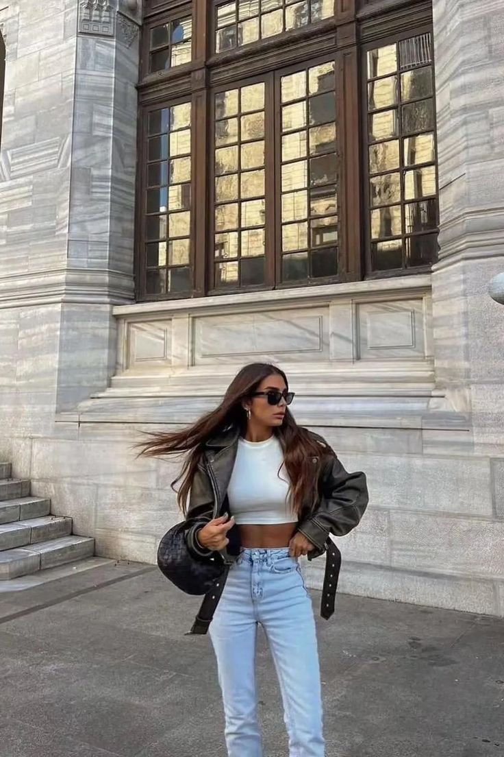 Woman in a leather jacket and crop top standing outdoors