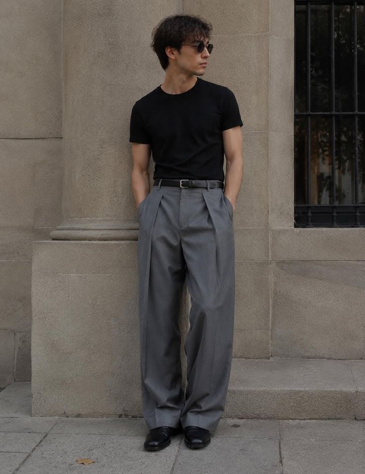 Man in a black t-shirt and grey pants leaning against a stone wall