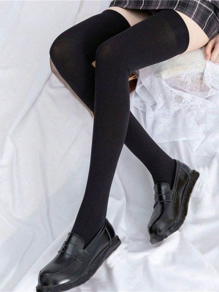 Person wearing thigh high socks, a plaid skirt, and black shoes on white bedding