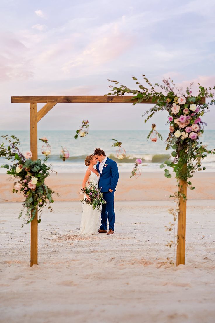 A couple embracing under a floral wedding arch on a beach