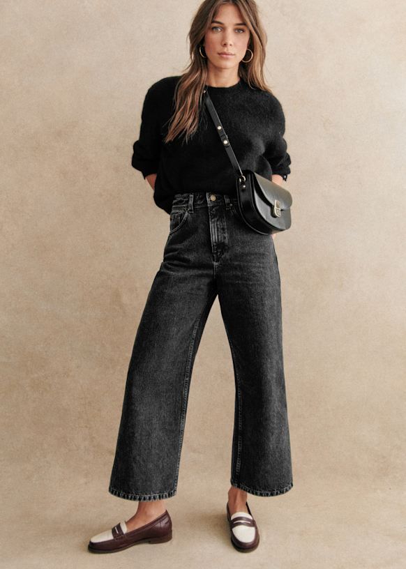 Woman in a black sweater and wide leg jeans with a shoulder bag