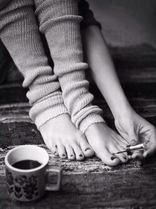 Person painting toenails while wearing leg warmers, with a coffee cup nearby