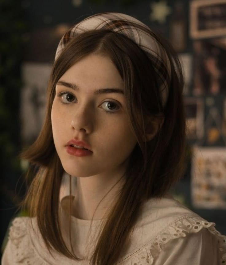 Young woman with brown hair and a plaid headband wearing a white top
