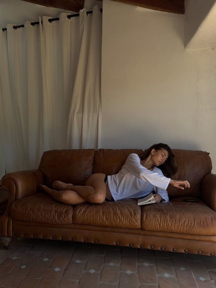 Woman in a white shirt and black underwear lying on a brown leather couch