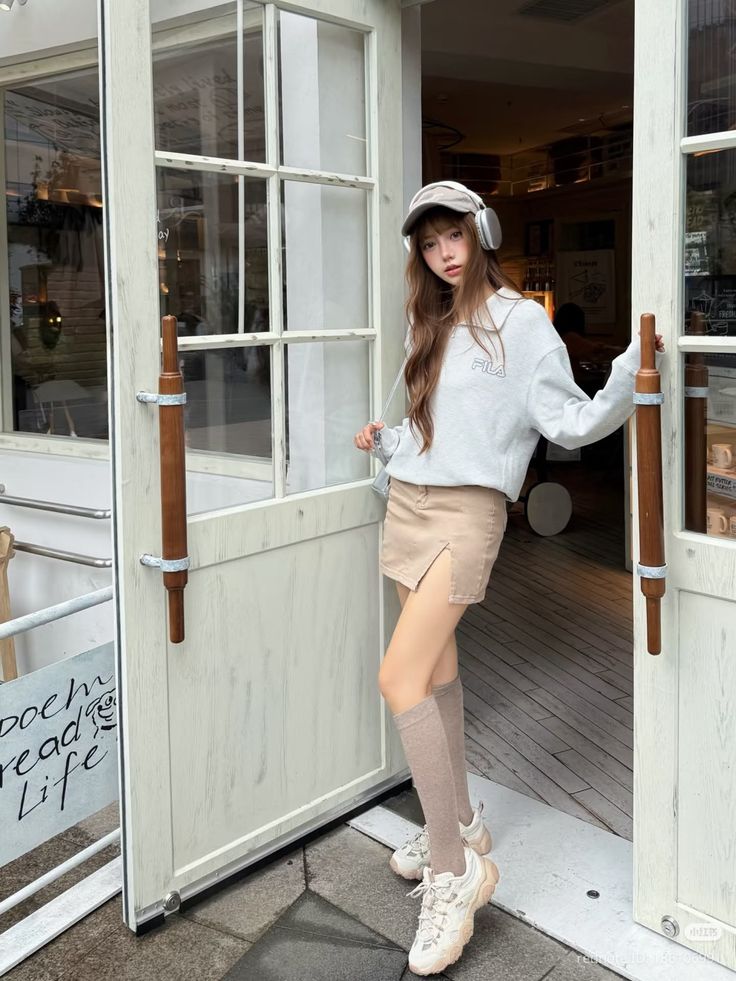 Woman in a sweatshirt and mini skirt with headphones and a cap standing in a doorway