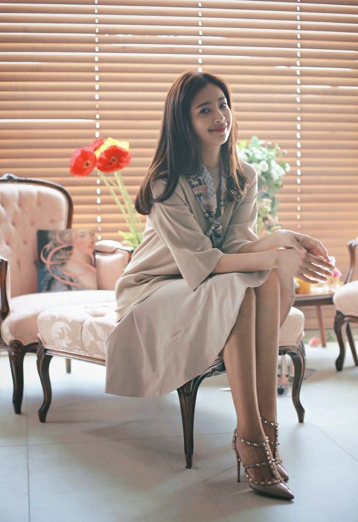 Woman with long hair in a beige dress and high heels sitting indoors