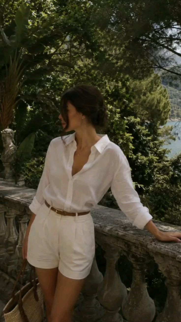 Woman in a white shirt and shorts leaning on a stone balcony outdoors