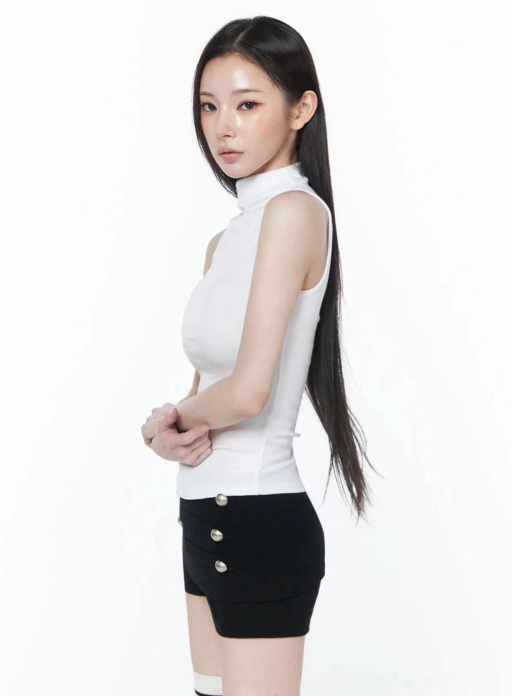 Woman with long black hair wearing a white turtleneck and black shorts in a studio