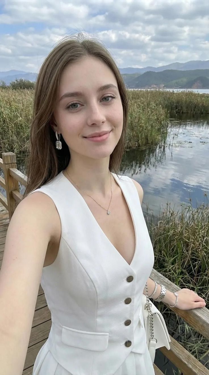 Woman in a white vest and jewelry on a wooden bridge by a lake