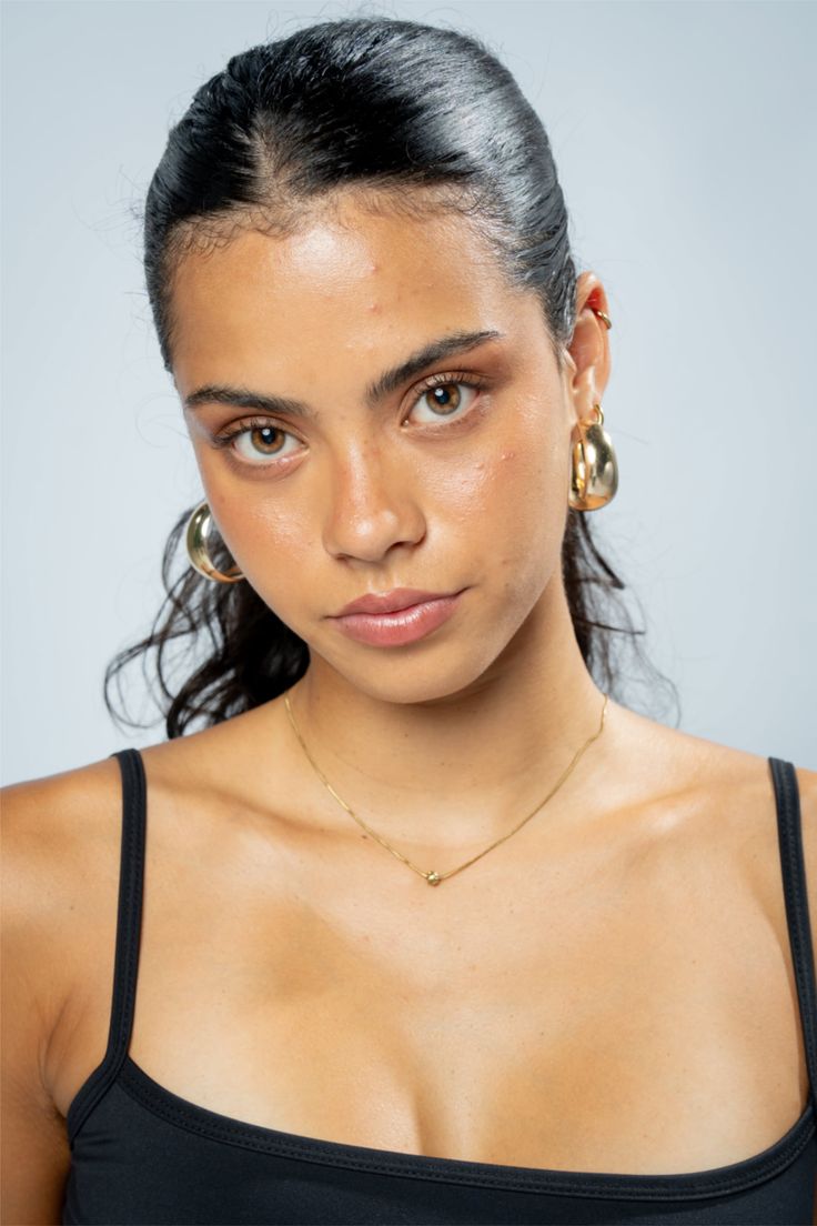 Woman with dark hair and gold jewelry in a studio portrait