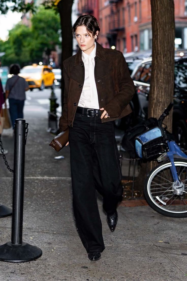 Person with short hair in a brown jacket and wide leg pants on a city street