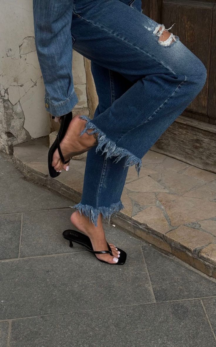 Person wearing ripped denim jeans with frayed hems and black sandals
