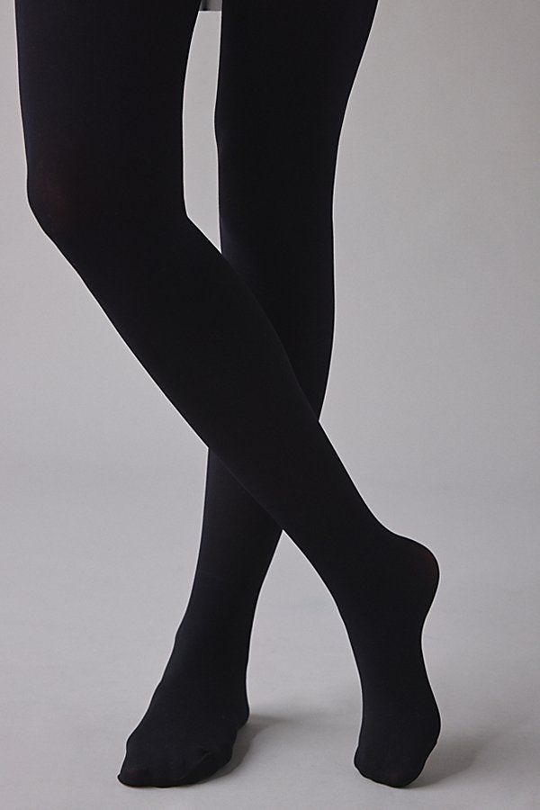 Person wearing black tights with legs crossed against a plain background