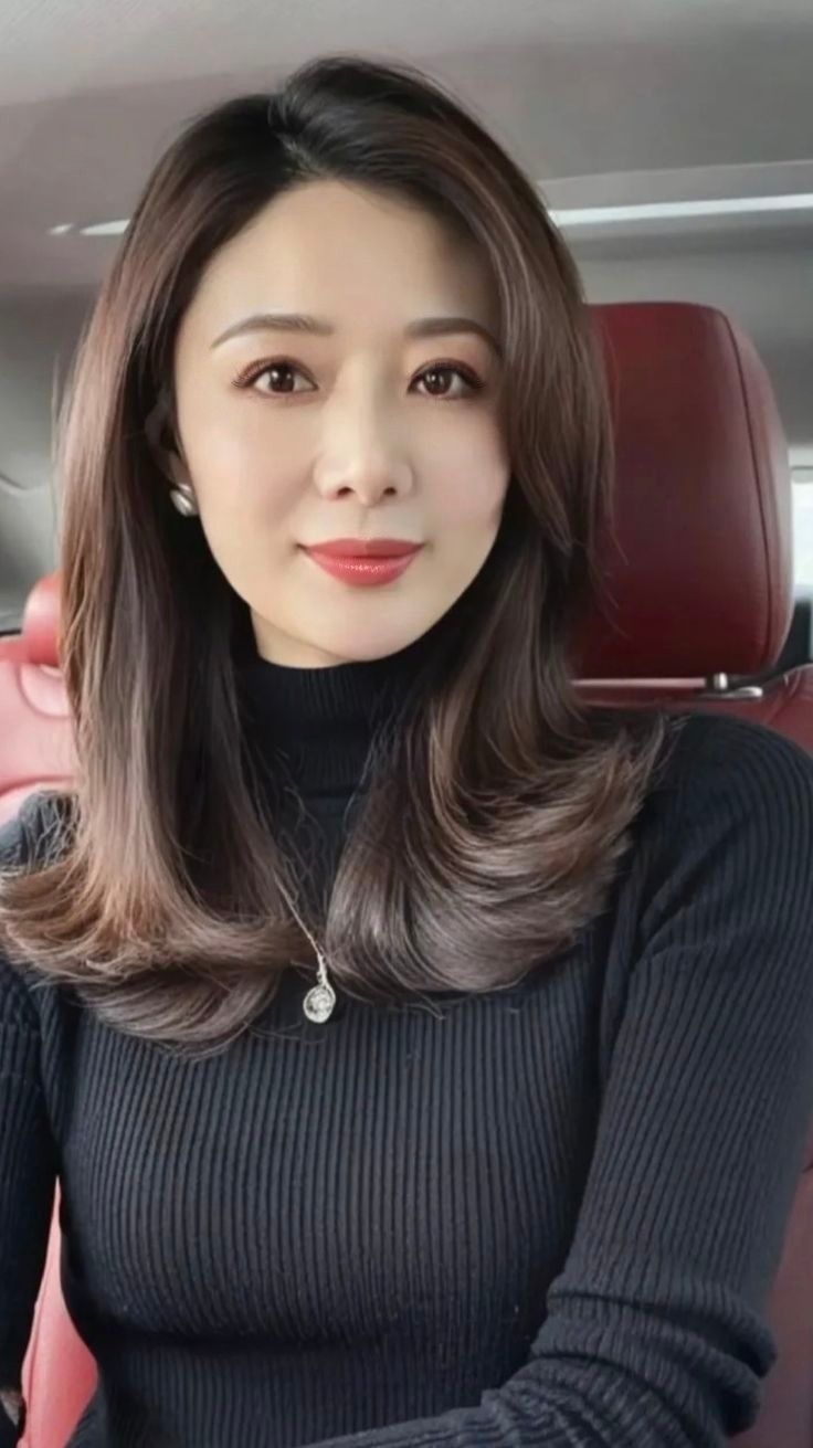Woman with long dark hair wearing a black turtleneck and necklace indoors