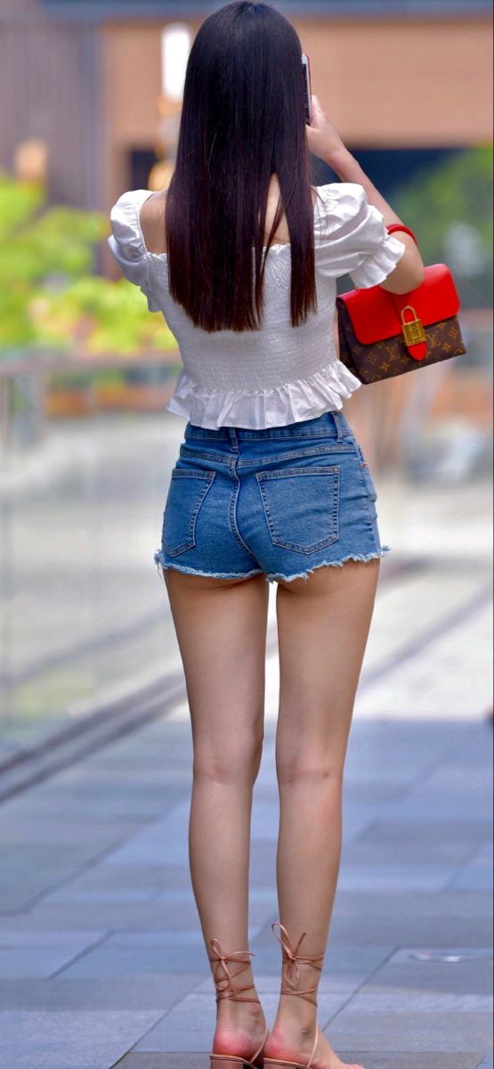 Woman in denim shorts and a white top from behind, holding a phone