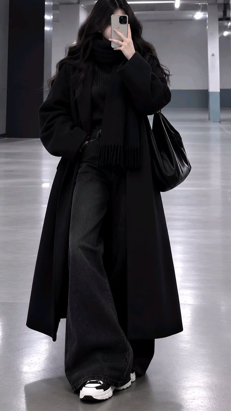 Person in a long black coat and wide leg jeans taking a mirror selfie