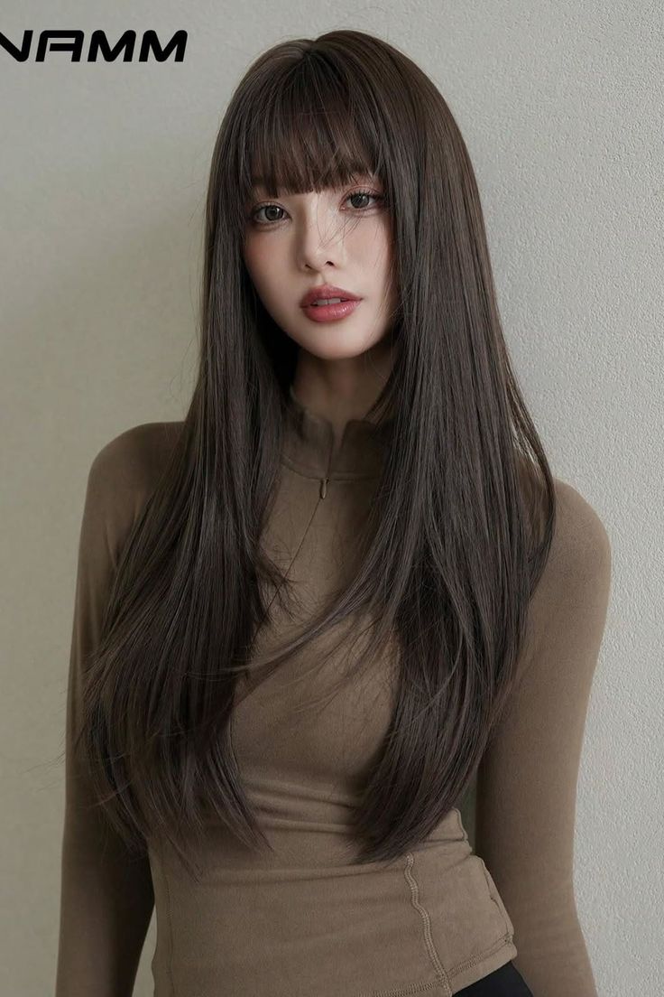 Woman with long brown hair and bangs wearing a brown long-sleeved top indoors