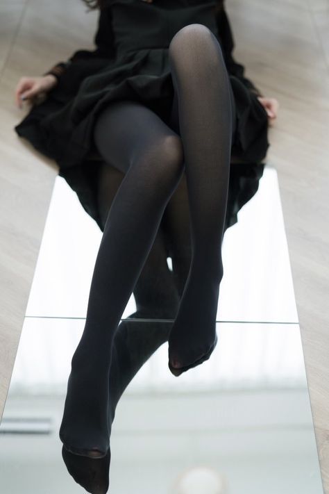 Person in a black dress and black tights with legs reflected in a mirror