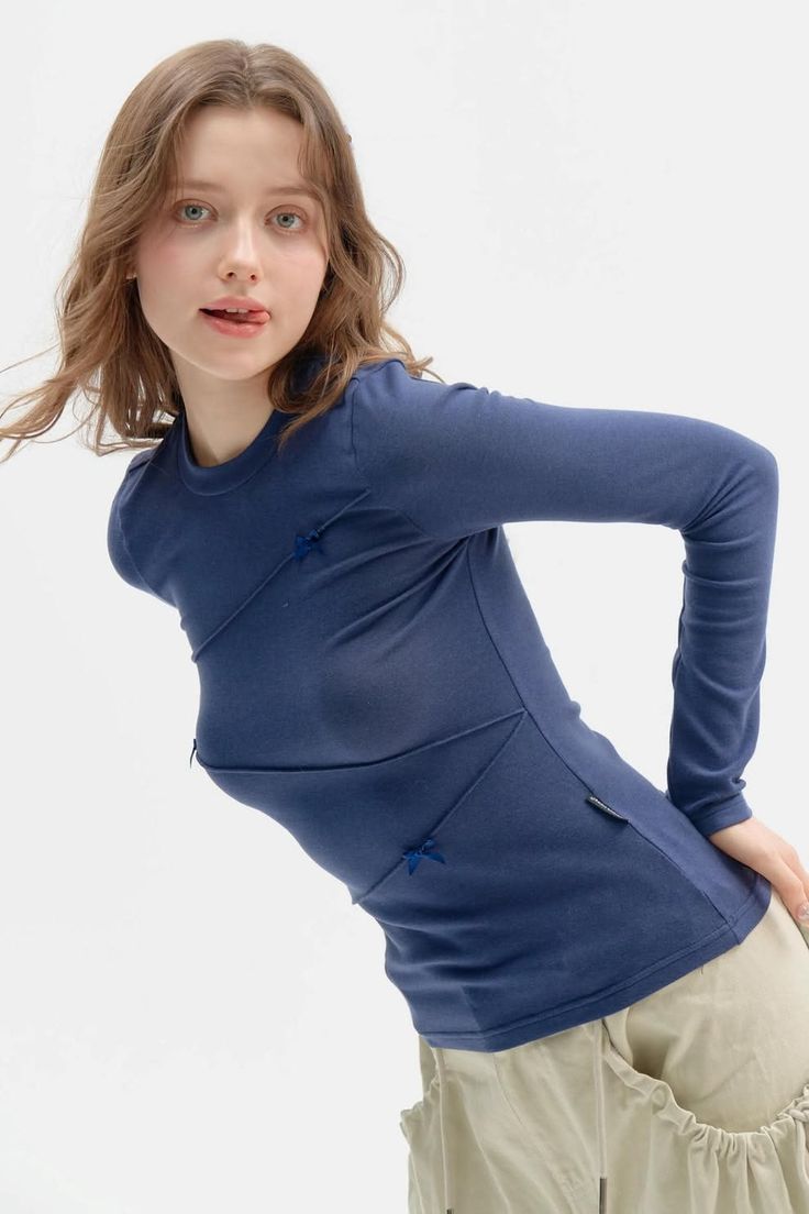 Woman in a blue long-sleeve shirt and beige pants with a playful expression