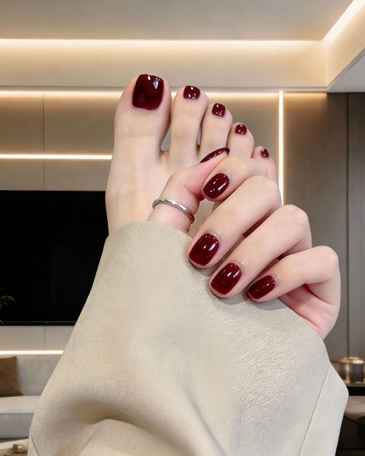 Hand and foot with matching red nail polish and a silver ring