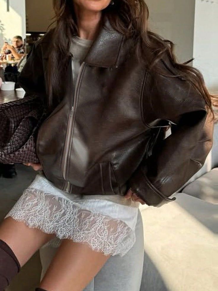 Woman in a brown leather jacket and white lace skirt indoors