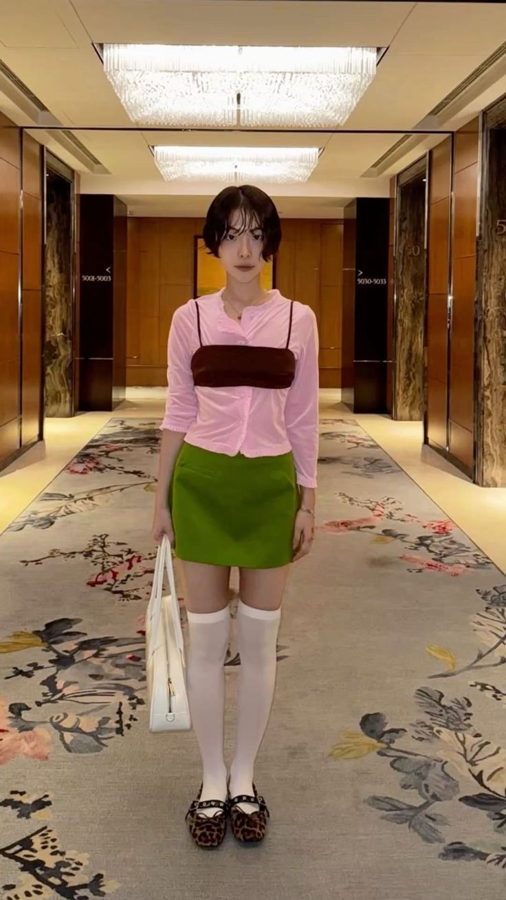 Woman with short hair in a pink cardigan and green skirt standing in a hallway