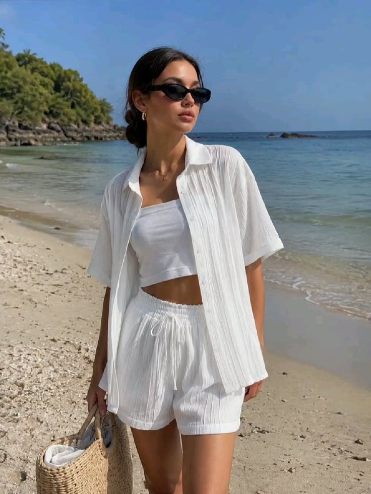Woman in a white outfit and sunglasses standing on a beach