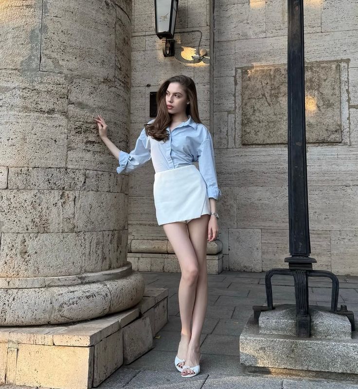 Woman in a blue shirt and white skirt posing next to a stone column