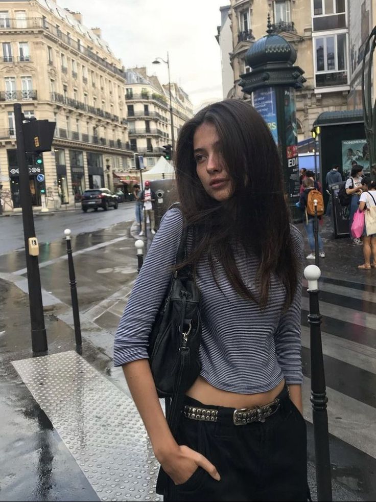 Woman with long dark hair wearing a striped shirt and studded belt on a city street