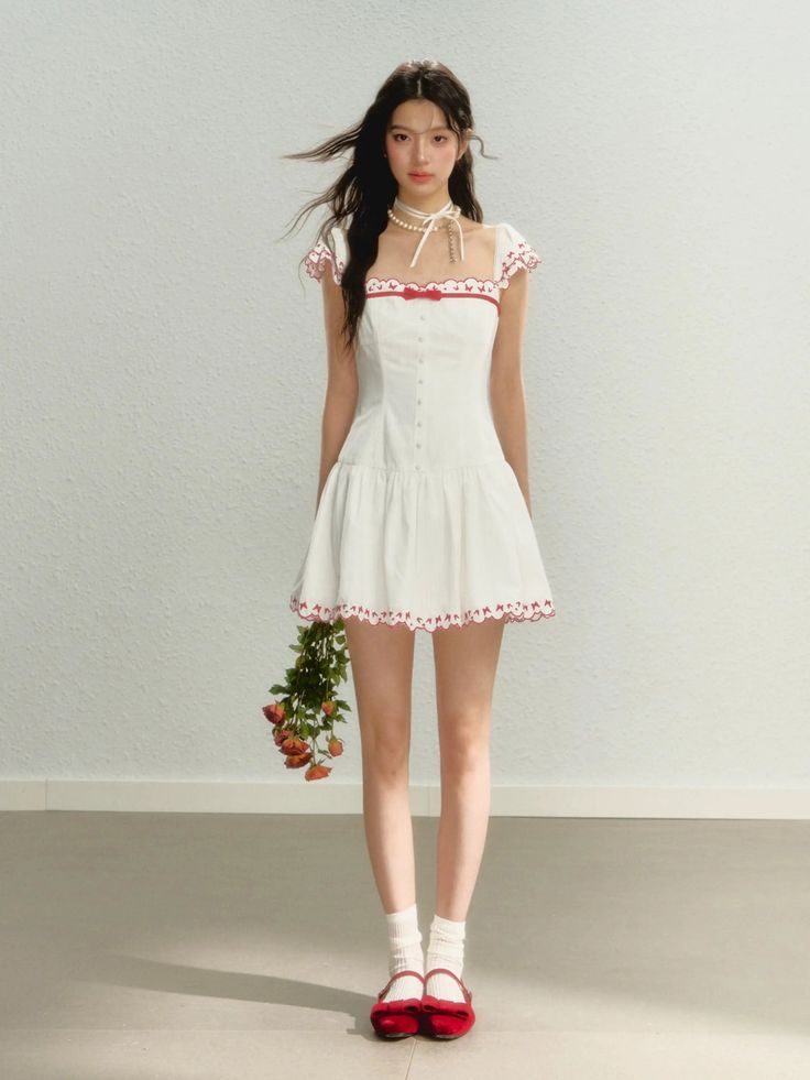 Woman in a white dress with red trim holding a bouquet of roses