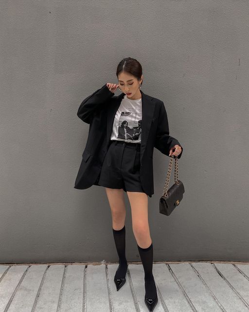 Woman in a black blazer and shorts with knee socks and pointed heels