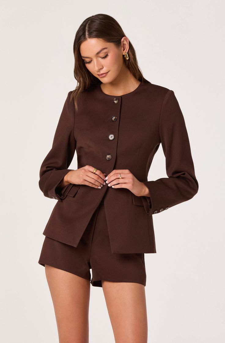Woman in a brown suit jacket and shorts against a white background