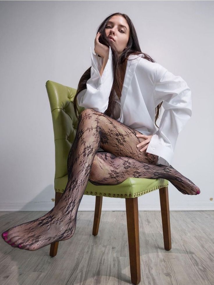 Woman in a white shirt and lace tights sitting on a green chair