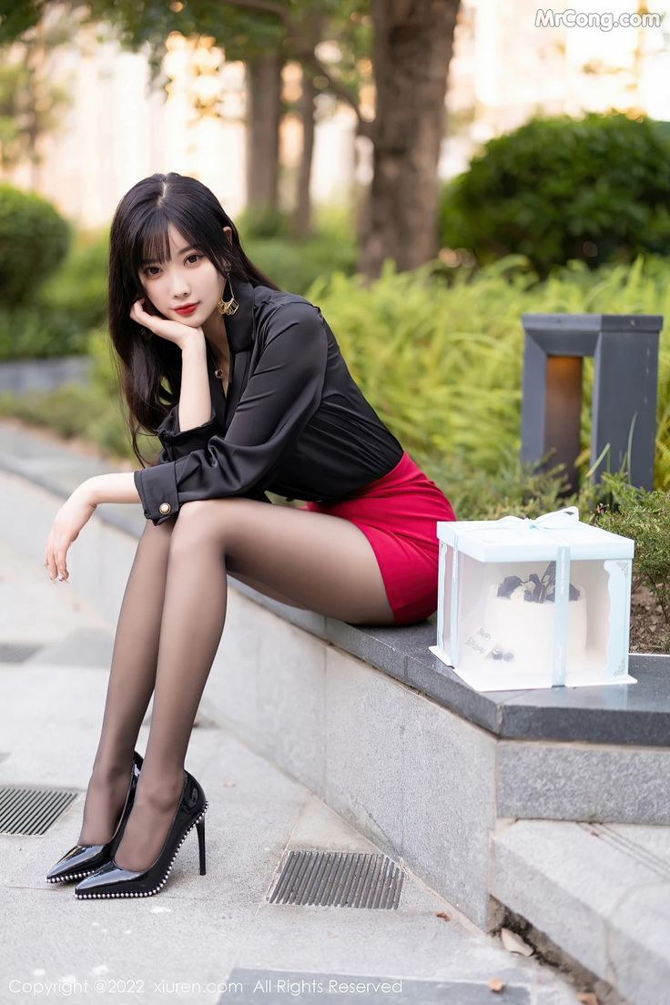 Woman in a red skirt and black shirt sitting outdoors with a birthday cake