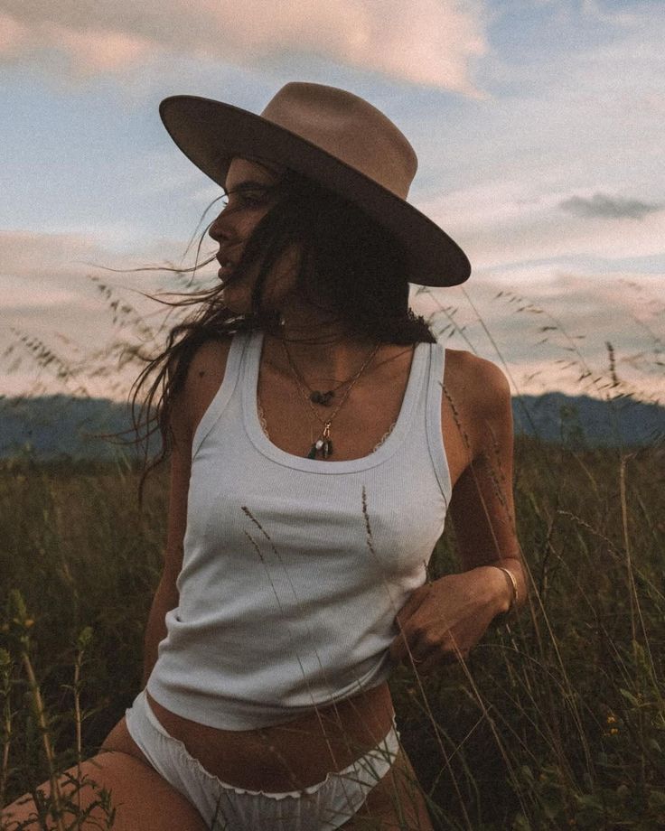 Woman in a tank top and underwear wearing a cowboy hat in tall grass