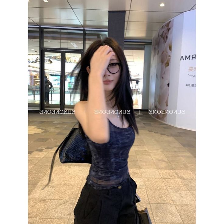 Woman with long black hair and glasses wearing a tank top and black pants indoors
