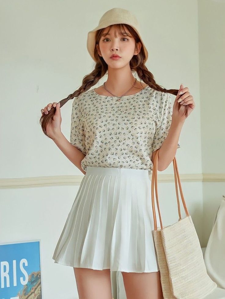 Woman with braids and a bucket hat wearing a floral top and pleated skirt