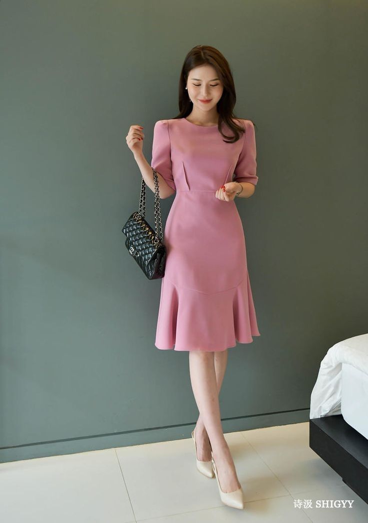 Woman in a pink dress holding a black handbag indoors