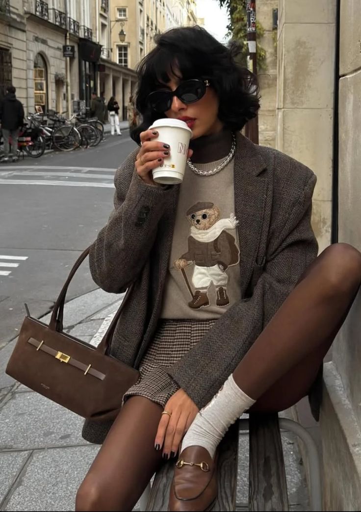 Woman in a blazer and plaid shorts drinking coffee on a city street