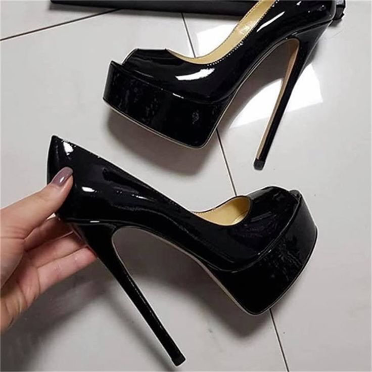 A hand holding a black patent leather platform high heel shoe