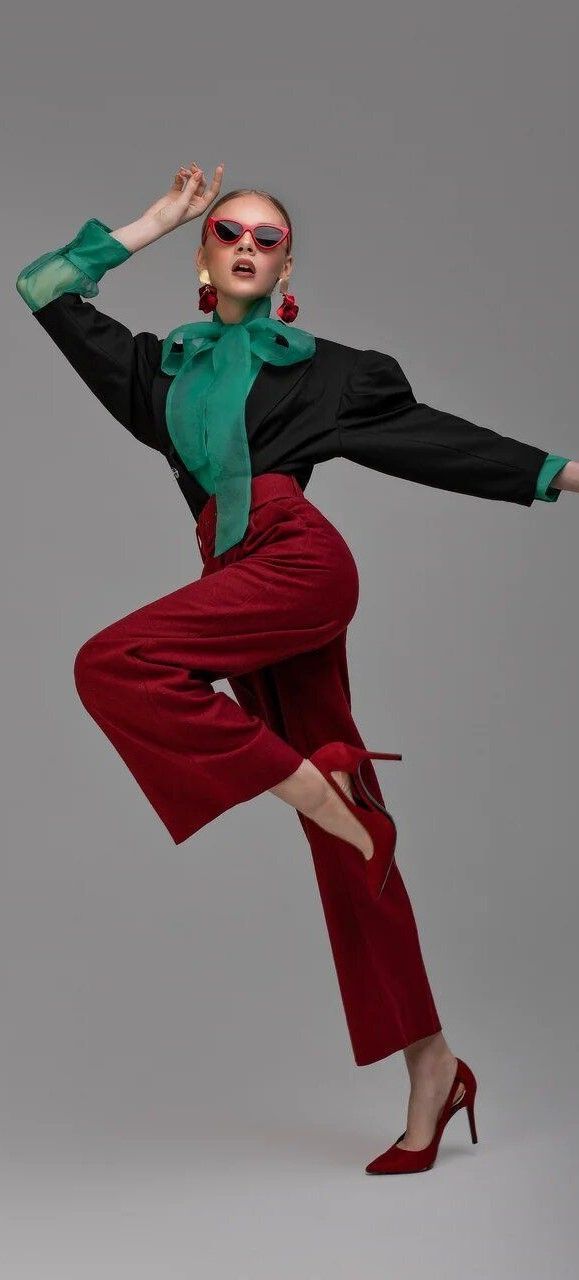 Woman in red pants, black top with green bow, and red sunglasses posing