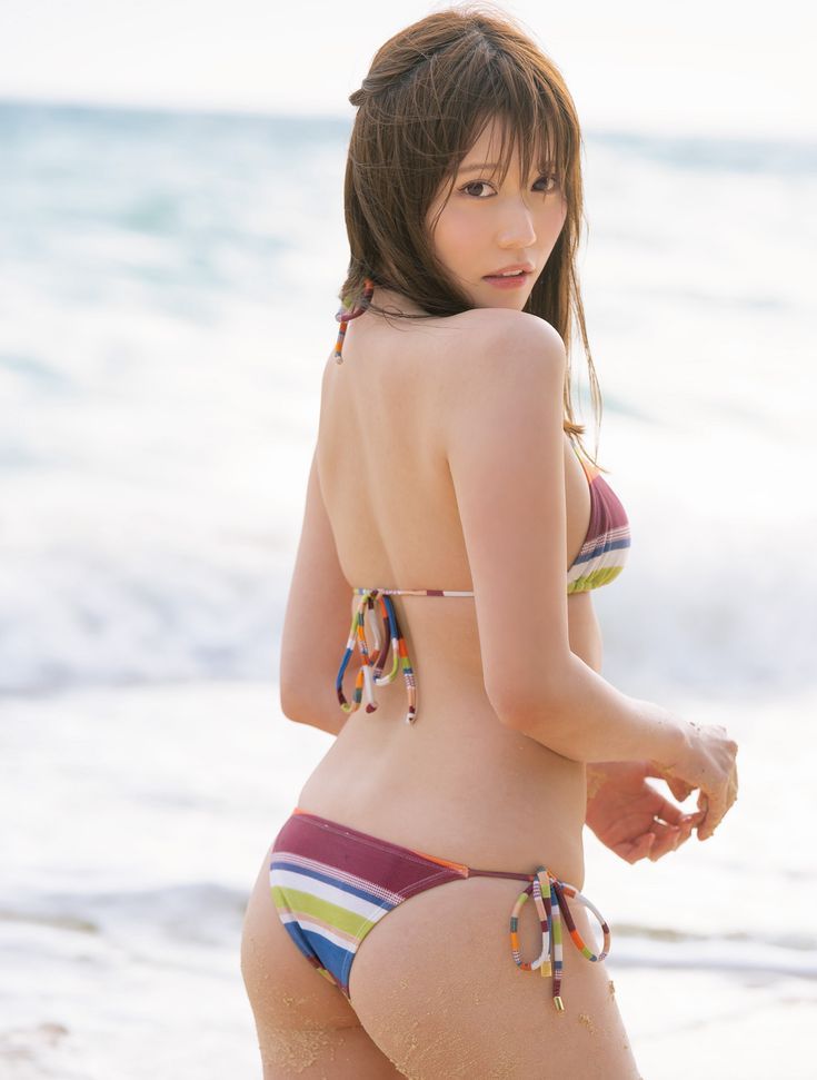 Woman in a striped bikini on a sandy beach, looking over her shoulder