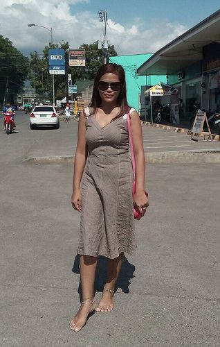 Woman in a midi dress and sunglasses standing barefoot on a street