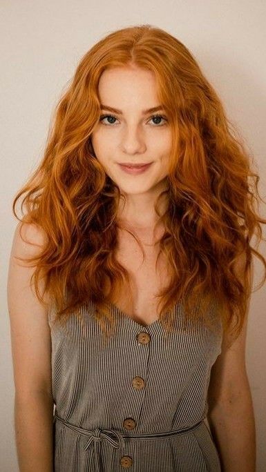 Woman with long wavy red hair wearing a striped dress with buttons