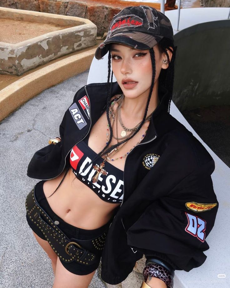 Woman in a crop top, racing jacket, and short shorts with braids and a camo hat