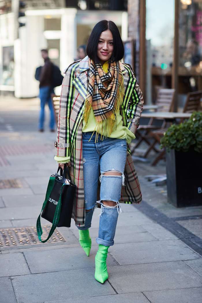 Woman in a plaid trench coat, ripped jeans, and neon green boots on a street