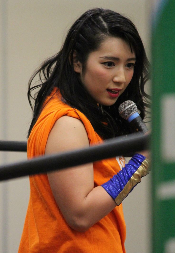 Woman with long black hair in an orange shirt holding a microphone